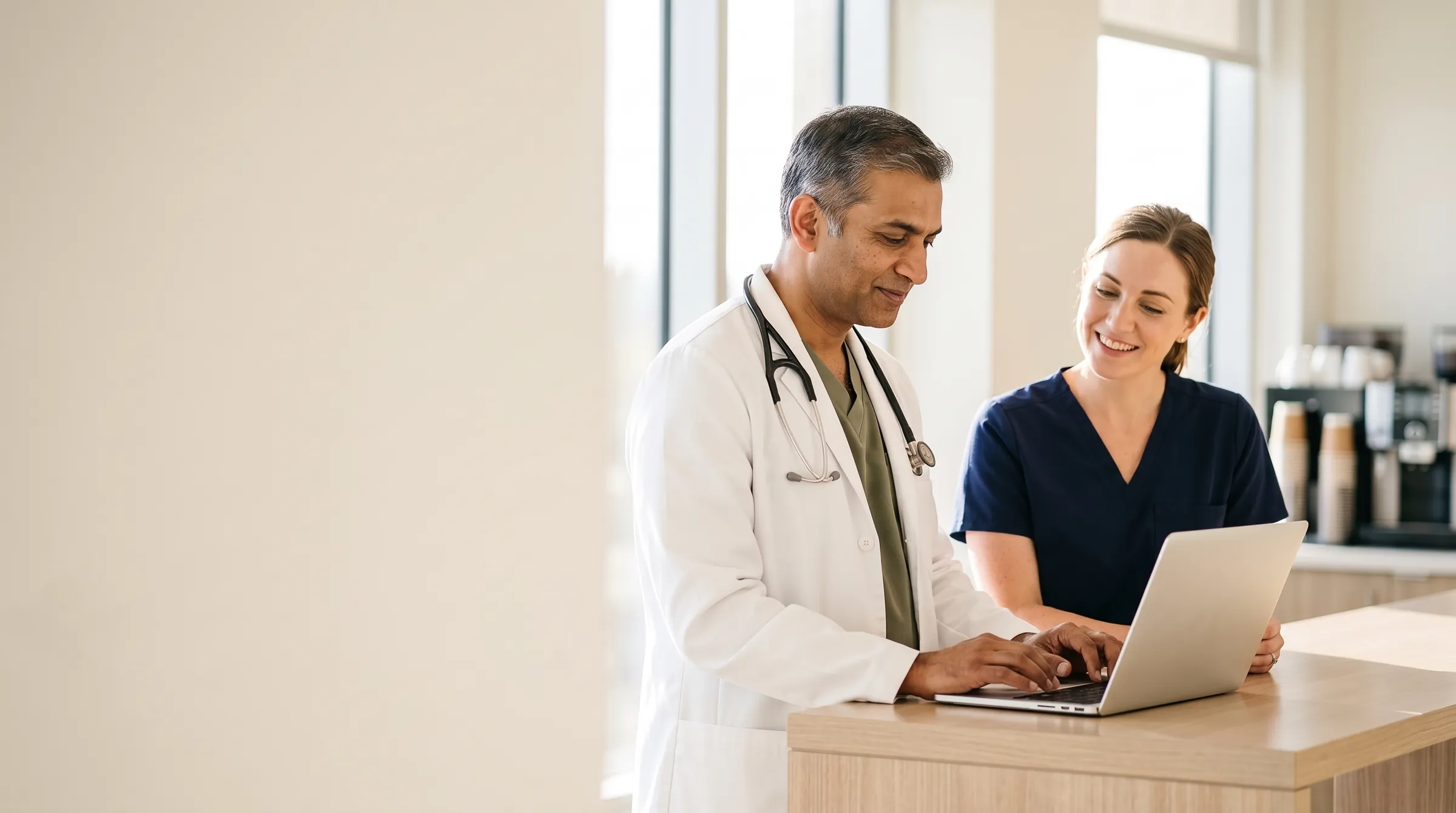 An emergency medical director and a newly hired attending going over her first schedule on a laptop in a bright workroom